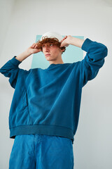 studio portrait on cyclorama of a young man with red curly hair in blue sweatshirt white beanie hat blue pants on blue paper background