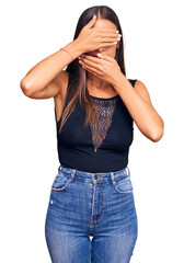 Young hispanic woman wearing casual clothes covering eyes and mouth with hands, surprised and shocked. hiding emotion
