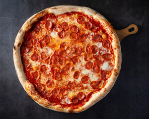 top view big pizza with salami on wooden cutting board. dark background
