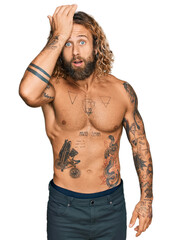 Handsome man with beard and long hair standing shirtless showing tattoos surprised with hand on head for mistake, remember error. forgot, bad memory concept.