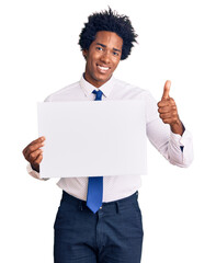 Handsome african american man with afro hair holding blank empty banner smiling happy and positive, thumb up doing excellent and approval sign