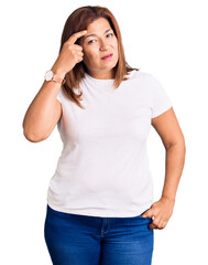 Middle age latin woman wearing casual white tshirt pointing unhappy to pimple on forehead, ugly...