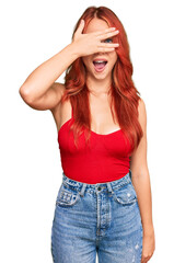 Young redhead woman wearing casual clothes peeking in shock covering face and eyes with hand, looking through fingers with embarrassed expression.