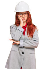 Young redhead woman wearing architect hardhat thinking looking tired and bored with depression problems with crossed arms.