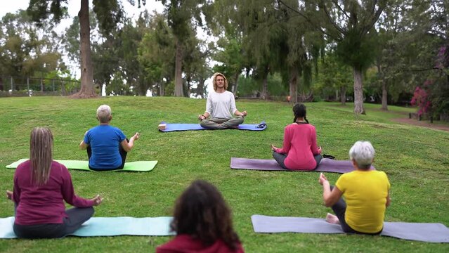Multiracial people with different ages doing yoga meditation exercise together at city park - Mental health and multi generational community concept
