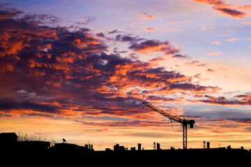 Naklejka premium Vibrant sunset over a silhouette of urban skyline with crane.