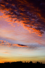 Fiery cloudscape at dusk above city buildings and silhouettes.