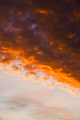 Dark clouds at sunset with fiery orange edges against a soft sky.