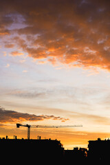 Sunset paints the sky with orange above a city silhouette and crane.