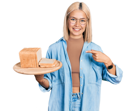 Beautiful young blonde woman holding bread pointing finger to one self smiling happy and proud