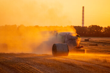 Combine harvester pressing straw from field into bales driving field on sunny summer evening. Field...