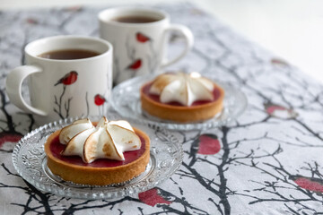 Tartlet cake with meringue and cups of tea on the table. Bullfinch pattern on tablecloths and cups....