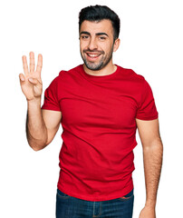 Naklejka premium Hispanic man with beard wearing casual red t shirt showing and pointing up with fingers number three while smiling confident and happy.