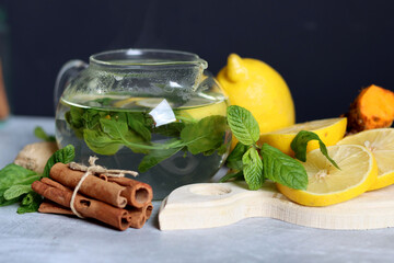 Still life with glass teapot, lemons and mint leaves on a table. Healthy homemade drink closes up...