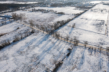 A road covered with snow among fields and meadows, view from a drone.