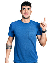 Young hispanic man wearing casual t shirt with a big smile on face, pointing with hand finger to the side looking at the camera.