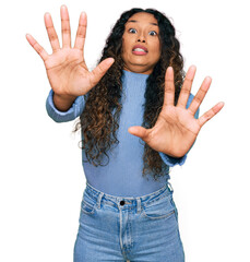 Young hispanic woman with curly hair wearing casual clothes afraid and terrified with fear expression stop gesture with hands, shouting in shock. panic concept.