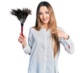 Beautiful caucasian woman holding cleaning duster pointing finger to one self smiling happy and proud