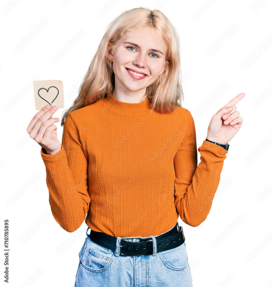 Sticker young caucasian woman holding heart reminder smiling happy pointing with hand and finger to the side