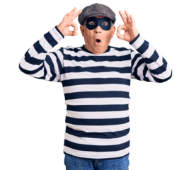 Senior handsome man wearing burglar mask and t-shirt looking surprised and shocked doing ok approval symbol with fingers. crazy expression