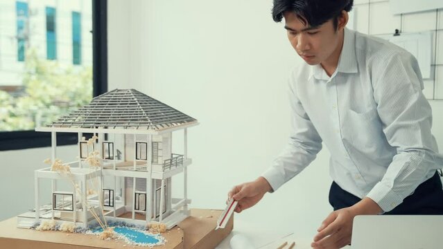 Close up of professional male architect engineer measure house model and using laptop analysis data at meeting table with house model and map . scatter around. Focus on hand. Immaculate.
