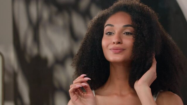 Mirror reflection beautiful pretty African American woman girl female lady fix curls check curly hair do hairdo hairstyle preparing morning beauty routine shampoo wink blink eye at camera flirting