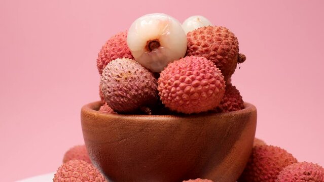 Lychee fruits in a wooden bowl , rotation in circle. tropical fruit lychee, Turning. selective focus. Lychee fruits on a pink background