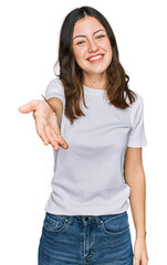 Young beautiful woman wearing casual white t shirt smiling cheerful offering palm hand giving assistance and acceptance.