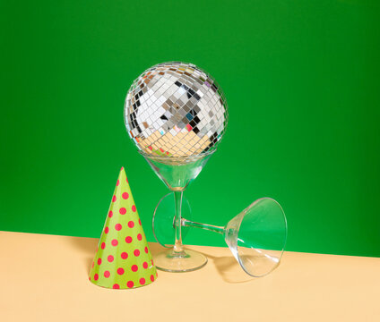 Mirrored glowing disco ball, wine or champagne glasses and a festive hat.