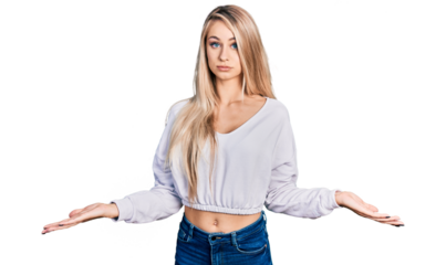Beautiful young blonde woman wearing casual white sweater clueless and confused expression with arms and hands raised. doubt concept.