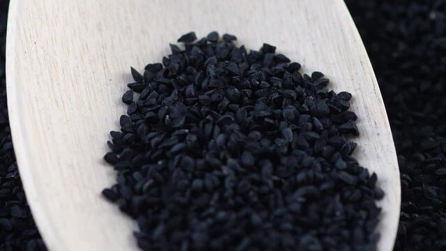 macro black cumin seeds on a wooden spoon rotation. black cumin harvest, use in cooking and medicine