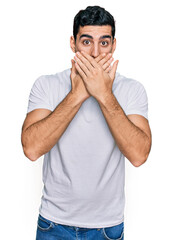 Fototapeta premium Handsome hispanic man wearing casual white t shirt shocked covering mouth with hands for mistake. secret concept.