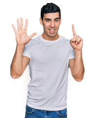 Naklejka premium Handsome hispanic man wearing casual white t shirt showing and pointing up with fingers number six while smiling confident and happy.