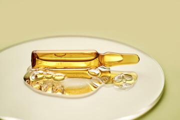 Ampoule in a drop of cosmetic gel on a green background.