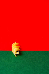 A single piece of fusilli pasta on a stark red and green color block backdrop