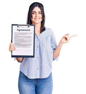 Young beautiful girl holding clipboard with agreement document smiling happy pointing with hand and finger to the side