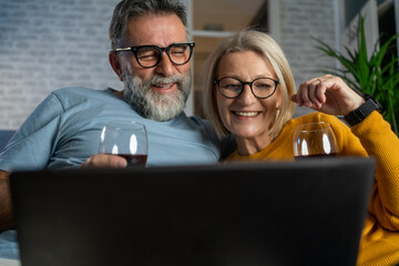 husband and wife enjoying good red wine at home while watching entertainment content on laptop