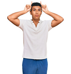 Young arab man wearing casual clothes doing funny gesture with finger over head as bull horns