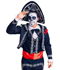 Young man wearing day of the dead costume over background very happy and smiling looking far away with hand over head. searching concept.