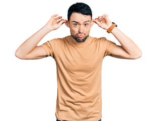 Hispanic man with beard wearing casual t shirt smiling pulling ears with fingers, funny gesture. audition problem