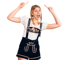 Young beautiful blonde woman wearing oktoberfest dress smiling amazed and surprised and pointing up with fingers and raised arms.