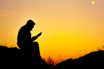 the silhouette of a man sitting on the ground and reading a book