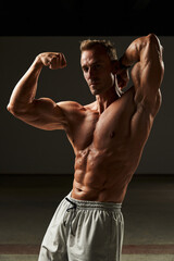  A symphony of sinew as a young, muscular man flexes, each muscle dancing in harmonious display, a true virtuoso of physicality, embodying the discipline and artistry of body sculpting.