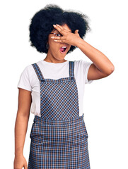 Young african american girl wearing casual clothes peeking in shock covering face and eyes with hand, looking through fingers with embarrassed expression.