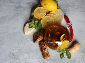 Teapot with hot tea, ginger, turmeric root, cinnamon sticks, lemon and mint leaves on grey background with copy space. Anti inflammatory winter drink recipe. 