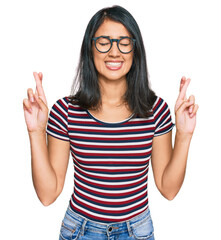 Beautiful asian young woman wearing casual clothes and glasses gesturing finger crossed smiling with hope and eyes closed. luck and superstitious concept.