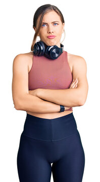 Beautiful caucasian young woman wearing gym clothes and using headphones skeptic and nervous, disapproving expression on face with crossed arms. negative person.