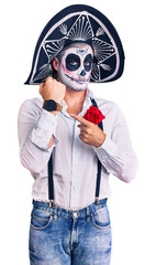 Man wearing day of the dead costume over background in hurry pointing to watch time, impatience, looking at the camera with relaxed expression