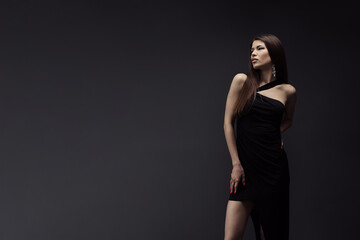 A woman stands confidently in a black dress, striking a pose for a portrait.