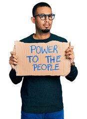 Young african american man holding power to the people banner clueless and confused expression. doubt concept.